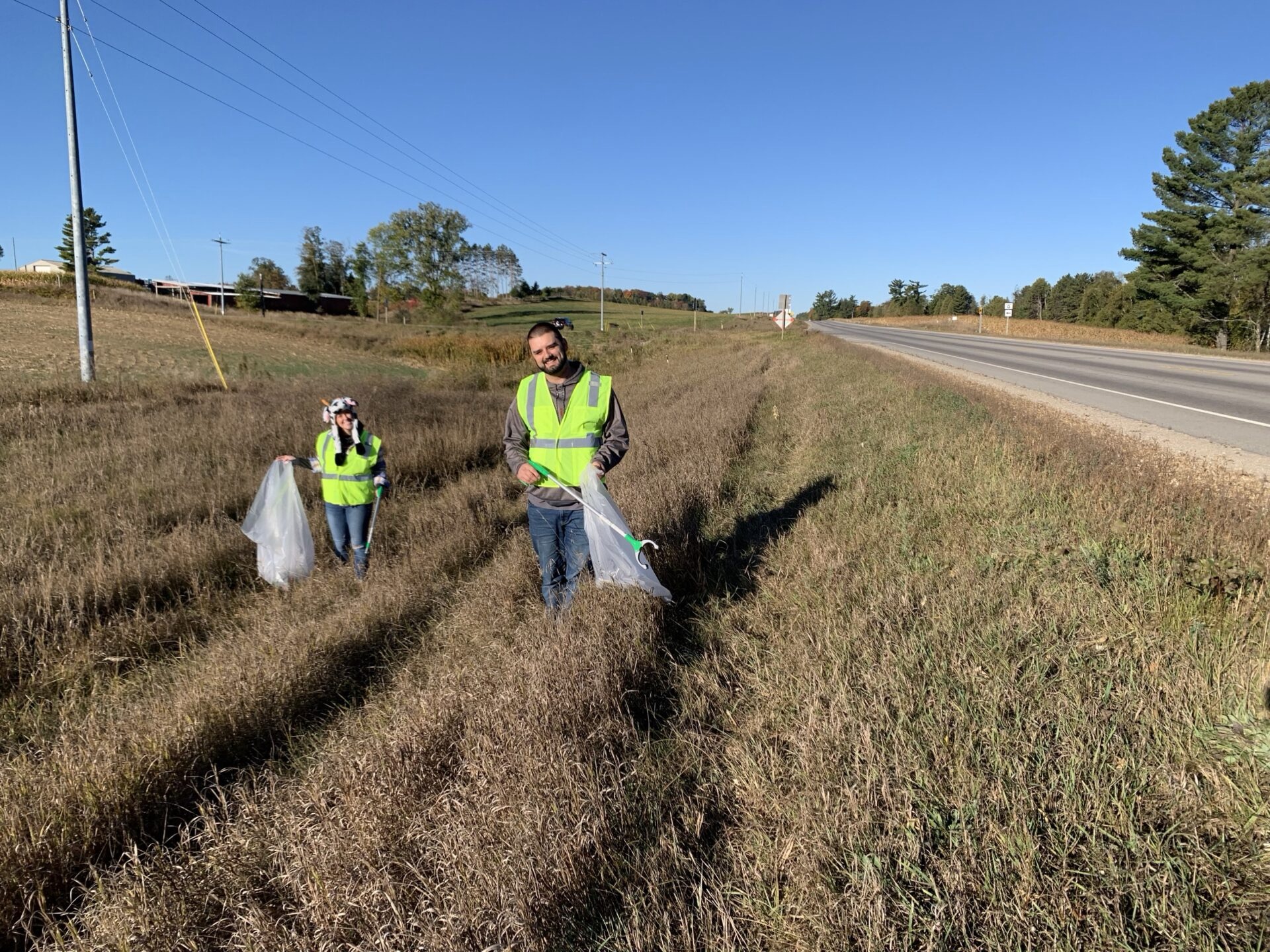Two Dairyland team members in safety vests picking up litter along a highway