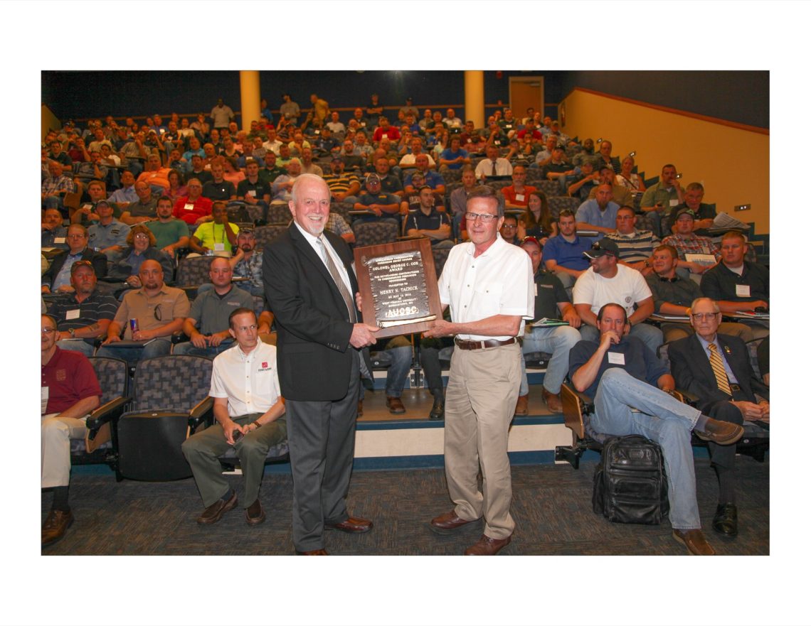 Henry Tachick holding an award plaque on stage